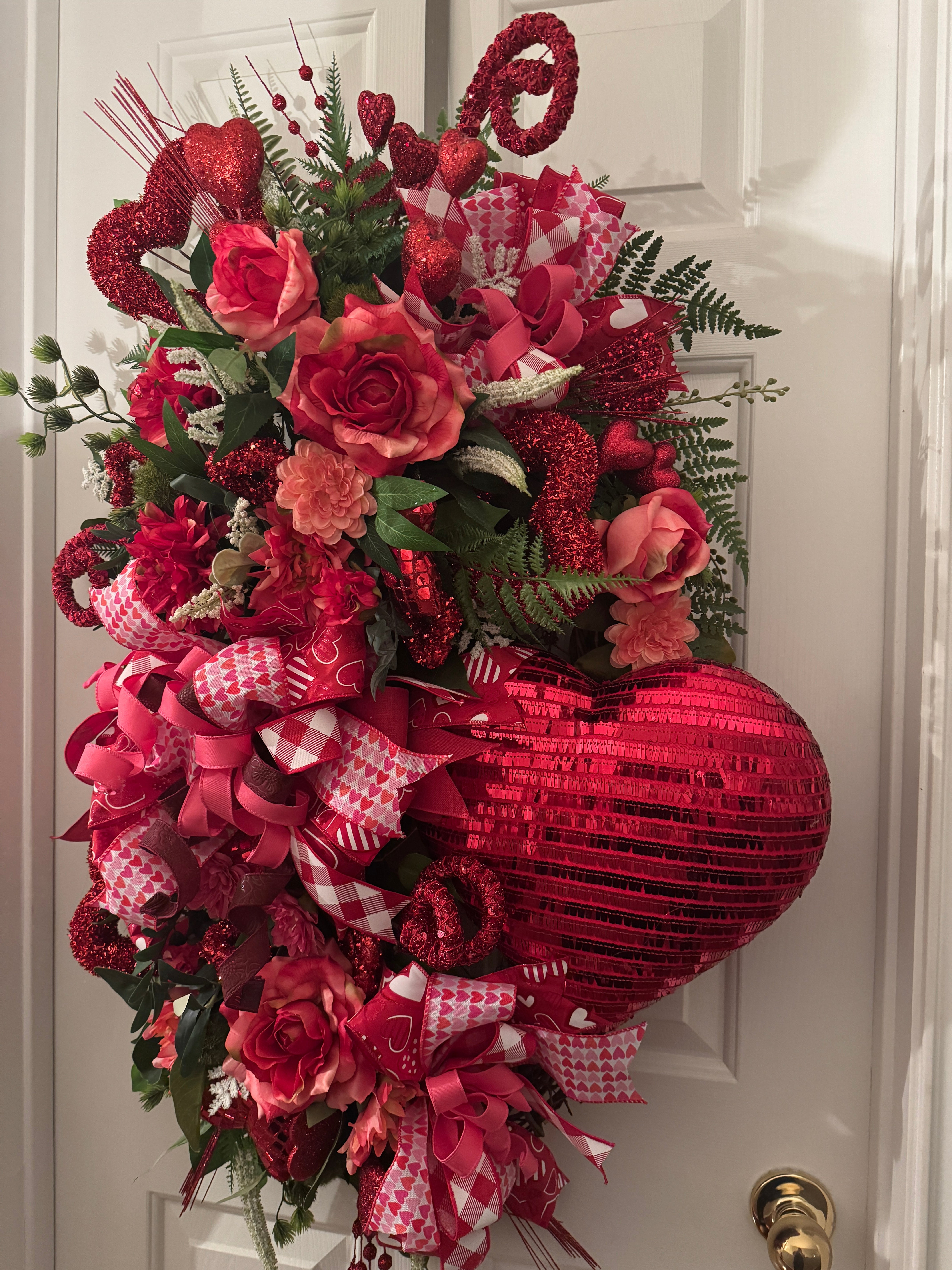 Beautiful large oval grapevine wreath in red and pink with large roses, a large sequined heart, greenery, and other adornments